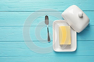 Dish with fresh butter and knife on wooden background