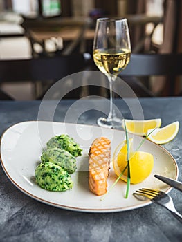 Dish with grilled salmon with lemon slices and glass of white wine on table. Close up view