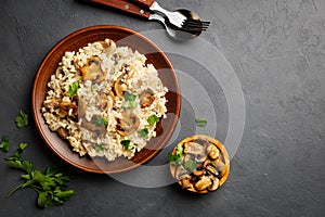 A dish of Italian cuisine - risotto from rice and mushrooms in a brown plate on a black slate background.