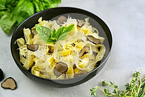 Dish of italian pasta fettuccine with sauce from truffle mushroom chips and green herbs served in a black bowl.