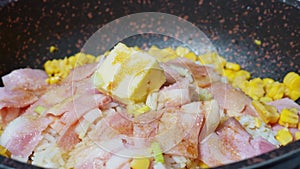 A dish made by frying cooked rice in oil. Woman cooking homemade fried rice with bacon, vegetables, butter and sweet corn in fryin