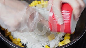 A dish made by frying cooked rice in oil. Woman cooking homemade fried rice with bacon, vegetables, butter and sweet corn in fryin