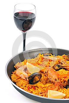 Dish of paella with a glass of red wine close-up on white background