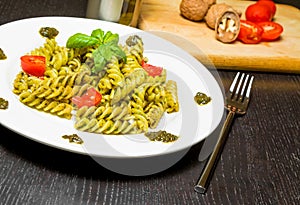 Dish of pasta with pesto genovese sauce and vegetables, tomato and basil on black wood table near fork