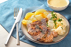 Dish with pork chop, cauliflower, potatoes and hollandaise sauce served with herb garnish on a plate and a blue napkin, selected