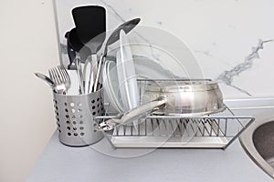 Dish rack with clean dry dishes and pan, different utensils on kitchen counter, washing and drying kitchenware