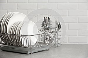 Dish rack with clean plates on table near brick wall