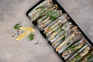 dish of razor clam grilled with garlic, parsley, olive oil and lemon slice on wood table