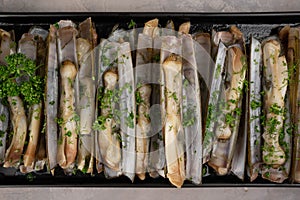 dish of razor clam grilled with garlic, parsley, olive oil and lemon slice on wood table