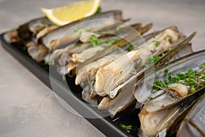 dish of razor clam grilled with garlic, parsley, olive oil and lemon slice on wood table