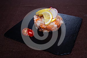 dish in the restaurant of red fish with lemon on a black plate.