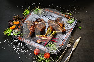 A dish with roasted quail meat with vegetables on black background