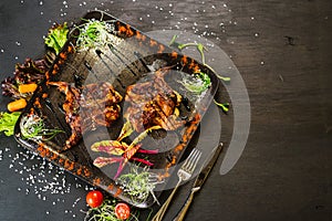 A dish with roasted quail meat with vegetables on black background