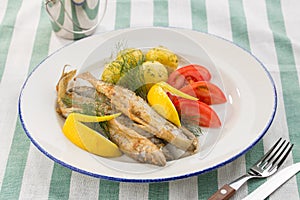 Dish with sardines fried, boiled potatoes, lemon and fresh tomatoes on textile background