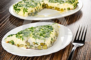Dish with section of omelet on background, slice of omelet with parsley and green peas in plate, fork on wooden table