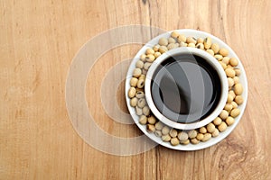 Dish of soy sauce with beans on wooden background, top view.