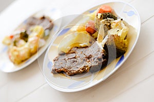 A dish of steak with carrots potato and brocoli on white table background