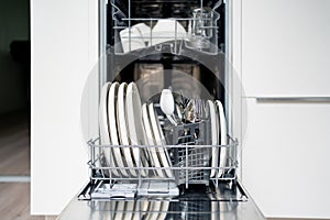 Dish washer machine. Washing plates and cutlery in basket. Open dishwasher in kitchen, front view. Full load of clean utensils.