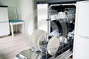 Dish washing machine. Washer in kitchen. Open dishwasher in modern white home. Full of clean plates.