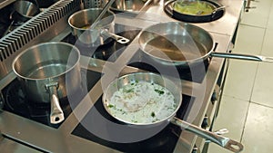 Dishes in frying pans being cooked on a stove while chef regulating temperature