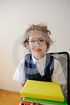 Disheveled little schoolboy holding a stack of textbooks and smiles.