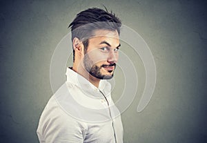 Dishonest man in white shirt looking with pretend smile at camera on gray background