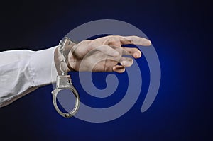 Dishonest and a prison doctor topic: the hand of man in a white shirt with handcuffs on a dark blue background in studio, put hand