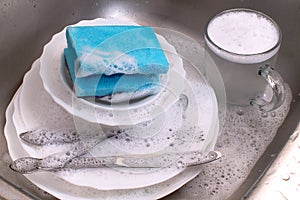 Dishware and utensils in kitchen sink with soap foam