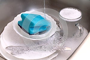 Dishware and utensils in kitchen sink with soap foam