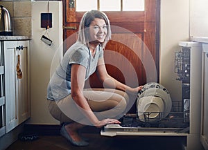 The dishwasher is every homemakers best friend. Portrait of a young woman using a dishwashing machine at home. photo