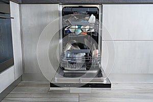 Dishwasher machine, open and loaded with dishes in the kitchen, after washing. Front view