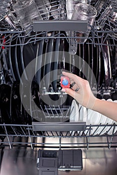 Dishwasher tablet in a woman& x27;s hands against the background of an open dishwasher
