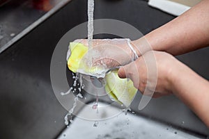 Dishwasher in uniform washes griddle with foam and sponge under the tap water