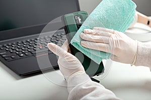 Disinfect phone with alcohol disinfectant. Woman in medical gloves wipes phone with tissue and disinfectant during covid 19.