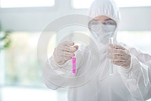 Disinfecting worker in protective workwear holding test tubes