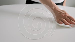 Disinfection concept - woman cleaning white table with wet wipe - slow motion