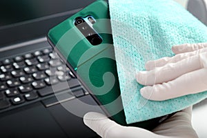 Disinfection phone and laptop keyboard by alcohol disinfectant. Woman in gloves wipes phone with tissue and disinfectant during