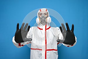 Disinfector man in a protective suit shows a ban on a blue isolated background, a disinfection service worker shows a stop gesture