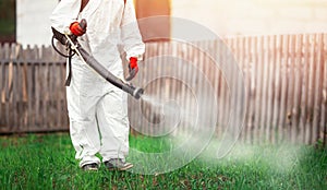 Disinfector in protective suit processes territory of garden plot of house sprays poison from mosquitoes, ticks and photo