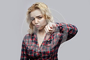 Dislike. Portrait of dissatisfied beautiful blonde young woman in casual red checkered shirt standing with thumbs down and looking