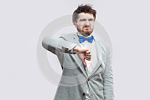 Dislike. Portrait of dissatisfied handsome bearded man in casual grey suit and blue bow tie standing and looking at camera with