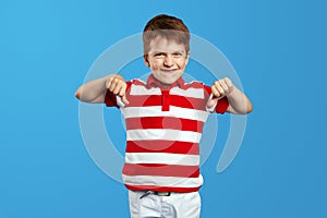 Little child boy in red striped shirt making disagree disapprove finger sign against blue background