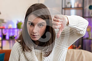 Upset young woman showing thumbs down, dislike bad work, disapproval, dissatisfied feedback at home