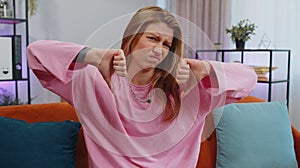Upset young woman showing thumbs down, dislike bad work, disapproval, dissatisfied feedback at home