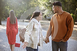 Disloyal man looking at another woman while walking with his girlfriend in park photo