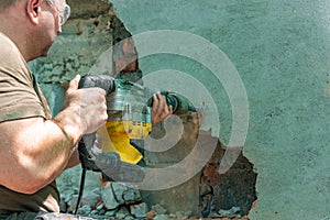 Dismantling walls and openings with an electric jackhammer. The worker in goggles performs repair work