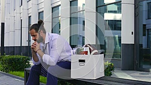 Dismissal and recruitment. An upset employee sits on a bench at a business center with a cortona box and personal items