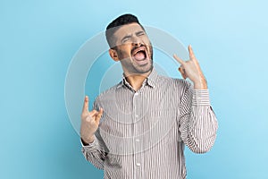 Disobedient businessman with beard showing rock and roll gesture and excitedly screaming, having fun