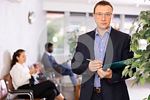 Dispassionate secretary man stands at reception with folder and list of guests and expects visitors
