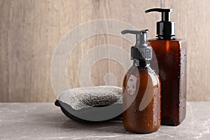 Dispenser bottles with water drops and bast wisp on beige marble table, space for text. Men`s cosmetics